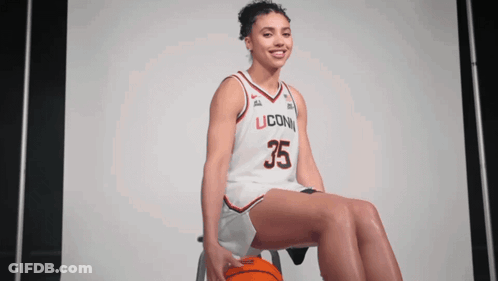 A Woman Wearing A Uconn Jersey Sits On A Stool With A Basketball GIF
