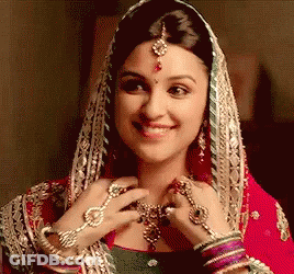 A Woman Wearing A Veil And Jewelry Is Smiling And Looking At Her Necklace . GIF