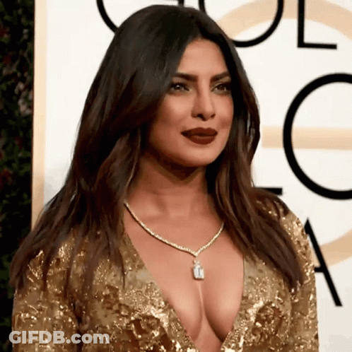 A Woman Wearing A Very Low Cut Gold Dress And A Necklace GIF