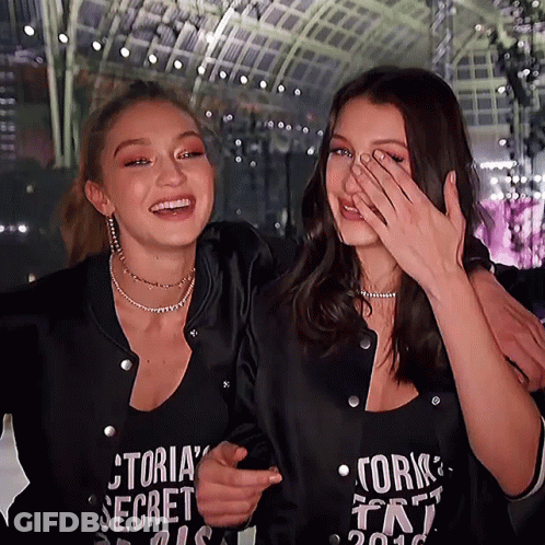 A Woman Wearing A Victoria 'S Secret Shirt Laughs With Another Woman GIF