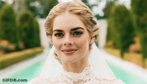 A Woman Wearing A Wedding Dress And Veil Smiles For The Camera GIF