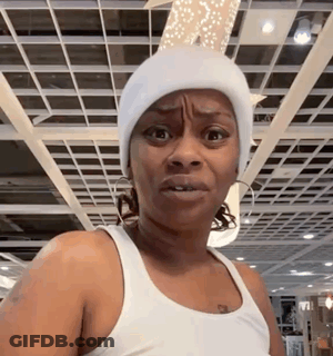 A Woman Wearing A White Beanie And A White Tank Top Is Making A Funny Face . GIF