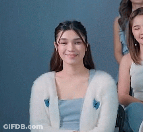 A Woman Wearing A White Cardigan With A Blue Butterfly On It Is Sitting Next To A Group Of Women . GIF
