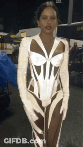 A Woman Wearing A White Corset And White Gloves Stands In Front Of A Blue Tarp GIF