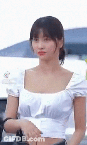 A Woman Wearing A White Crop Top Is Standing In Front Of A Car . GIF
