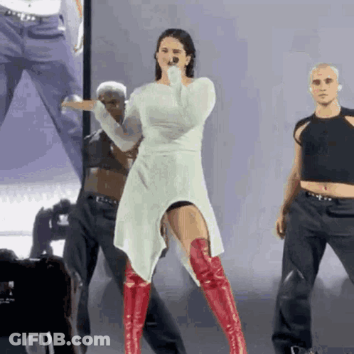 A Woman Wearing A White Dress And Red Boots Is Singing Into A Microphone . GIF