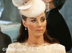 A Woman Wearing A White Hat And Veil Is Looking At The Camera . GIF