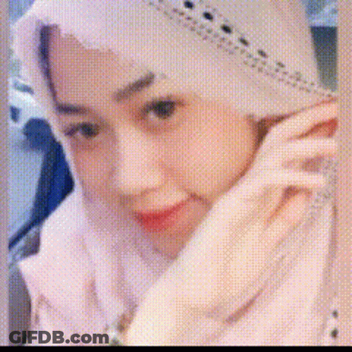 A Woman Wearing A White Hijab And A White Jacket Is Talking On A Cell Phone . GIF
