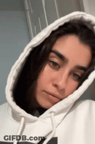 A Woman Wearing A White Hoodie With A Nose Ring Looks At The Camera . GIF