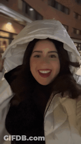 A Woman Wearing A White Jacket With A White Hood Is Smiling GIF