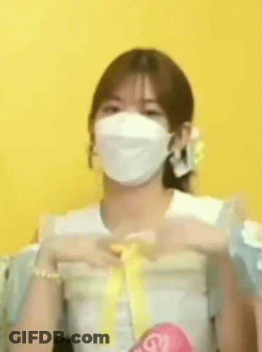 A Woman Wearing A White Mask Is Making A Heart Shape With Her Hands . GIF
