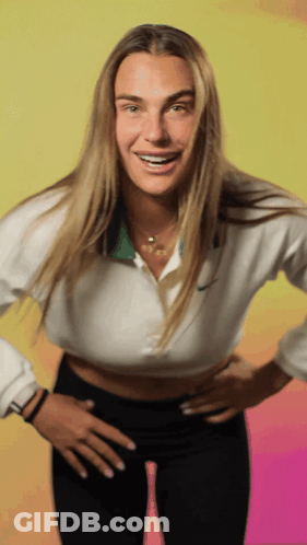 A Woman Wearing A White Nike Shirt And Black Pants Smiles With Her Hands On Her Hips GIF