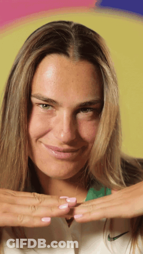 A Woman Wearing A White Nike Shirt Is Smiling With Her Hands On Her Chest GIF