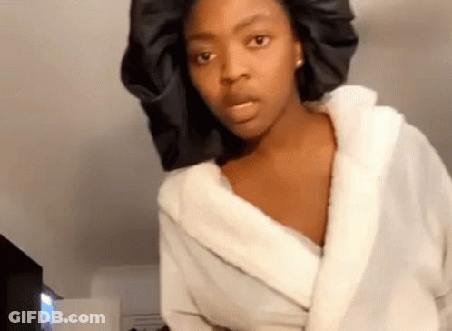 A Woman Wearing A White Robe And A Black Hat Is Making A Funny Face . GIF