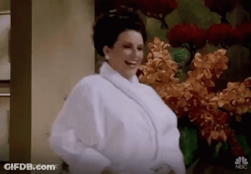 Woman In White Robe Standing In Front Of Flowers GIF