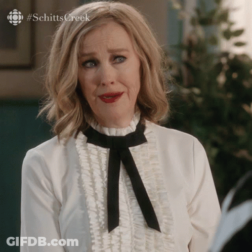 A Woman Wearing A White Shirt And A Black Bow Tie With #Schitts Creek On The Bottom GIF