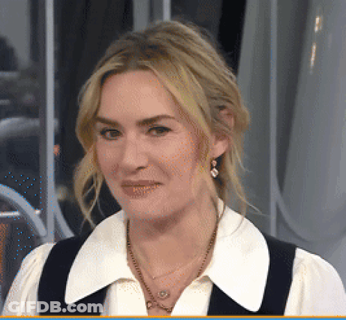 A Woman Wearing A White Shirt And A Black Vest Is Smiling GIF