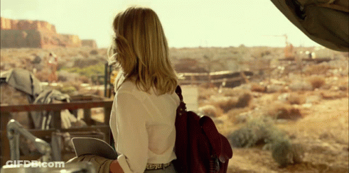 A Woman Wearing A White Shirt And A Brown Bag Looks Out Over A Desert Landscape GIF