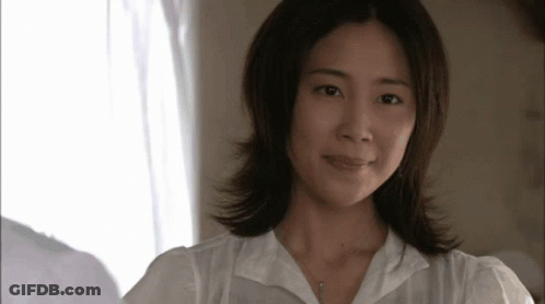 A Woman Wearing A White Shirt And A Necklace Looks At The Camera GIF