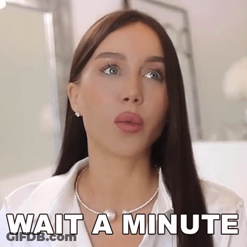 A Woman Wearing A White Shirt And A Necklace Says Wait A Minute . GIF