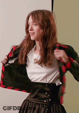 A Woman Wearing A White Shirt And A Plaid Jacket Takes Off Her Jacket GIF