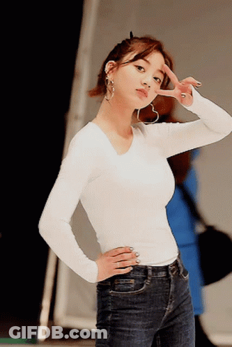 A Woman Wearing A White Shirt And Blue Jeans Is Giving A Peace Sign GIF