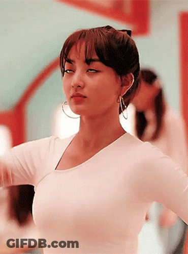 A Woman Wearing A White Shirt And Hoop Earrings Is Standing In Front Of A Mirror GIF