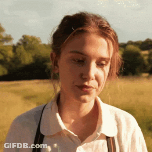 A Woman Wearing A White Shirt And Suspenders Looks Down GIF