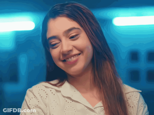 A Woman Wearing A White Shirt Is Smiling And Looking At The Camera GIF