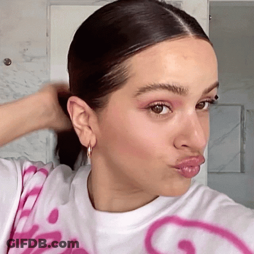 A Woman Wearing A White Shirt With A Pink Smiley Face On It Makes A Funny Face GIF