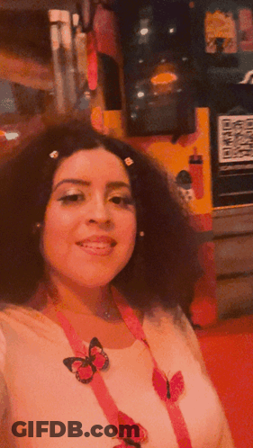 A Woman Wearing A White Shirt With Pink Butterflies On It Is Smiling GIF