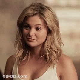 A Woman Wearing A White Tank Top Looks At The Camera GIF