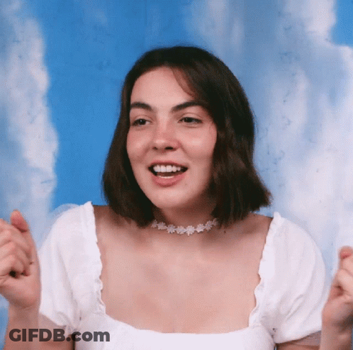 A Woman Wearing A White Top And A Choker Smiles With Her Hands In The Air GIF