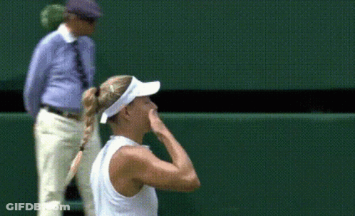 A Woman Wearing A White Visor Stands On A Tennis Court With Her Hand To Her Face GIF