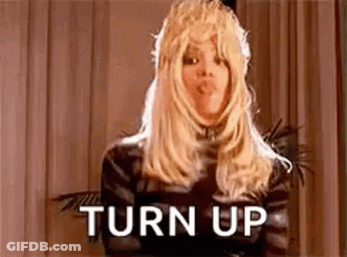 A Woman Wearing A Wig And A Crown Is Standing In Front Of A Curtain . GIF