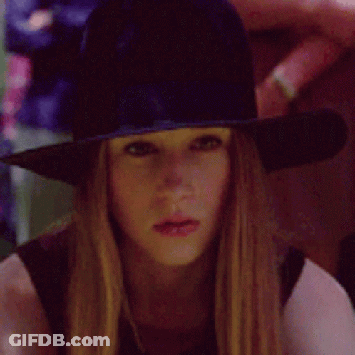 A Woman Wearing A Witch Hat Is Looking At The Camera GIF