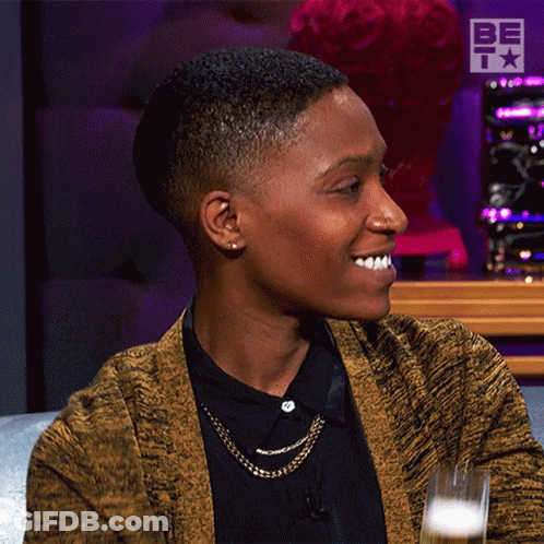 A Woman Wearing A Yellow Cardigan And A Black Shirt Is Smiling GIF