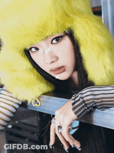 A Woman Wearing A Yellow Furry Hat And Striped Shirt GIF