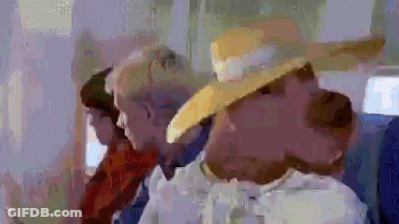 A Woman Wearing A Yellow Hat Is Sitting Next To A Man In A Suit On A Plane . GIF