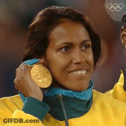 A Woman Wearing A Yellow Jacket Is Holding A Gold Medal Around Her Neck GIF