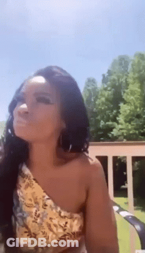 A Woman Wearing A Yellow One Shoulder Top And Earrings Is Sitting On A Lawn Chair . GIF