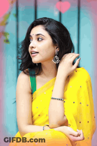 A Woman Wearing A Yellow Saree And Earrings Is Looking To The Side GIF