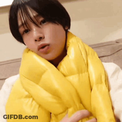 A Woman Wearing A Yellow Scarf Around Her Neck Looks At The Camera GIF