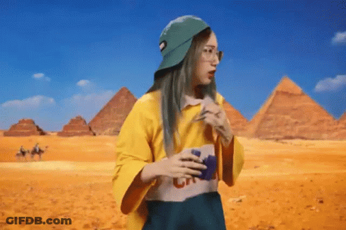 A Woman Wearing A Yellow Shirt And A Green Hat Is Standing In Front Of Pyramids . GIF