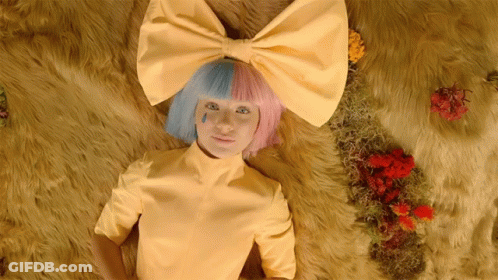 A Woman Wearing A Yellow Shirt And A Pink And Blue Bow On Her Head GIF