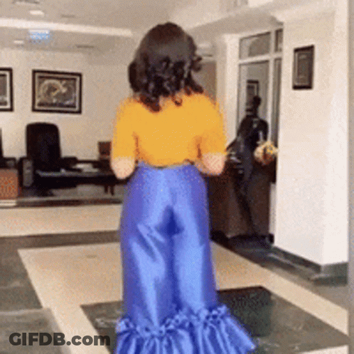 A Woman Wearing A Yellow Shirt And Blue Pants Is Standing In A Living Room GIF