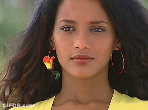 A Woman Wearing A Yellow Shirt And Red Hoop Earrings Looks At The Camera GIF