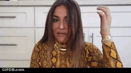 A Woman Wearing A Yellow Snake Print Shirt Is Holding Her Hair . GIF