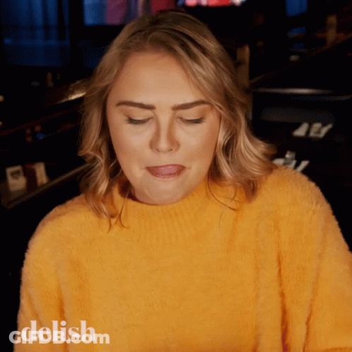 A Woman Wearing A Yellow Sweater With The Word Delish On The Bottom Left GIF