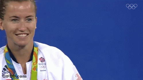 A Woman Wearing An Adidas Jacket Is Holding A Gold Medal In Front Of Her Face GIF